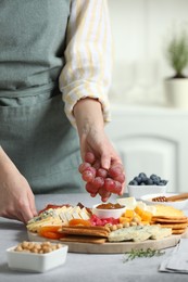 Photo of Woman serving antipasto platter with different types of cheese and other snacks with grapes at grey textured table indoors, closeup