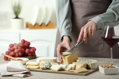 Photo of Woman slicing delicious cheese at light textured table indoors, closeup