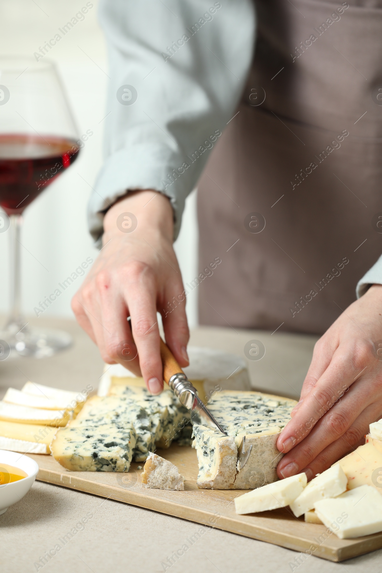 Photo of Woman slicing delicious cheese at light textured table indoors, closeup