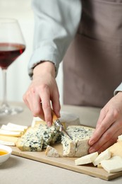 Photo of Woman slicing delicious cheese at light textured table indoors, closeup