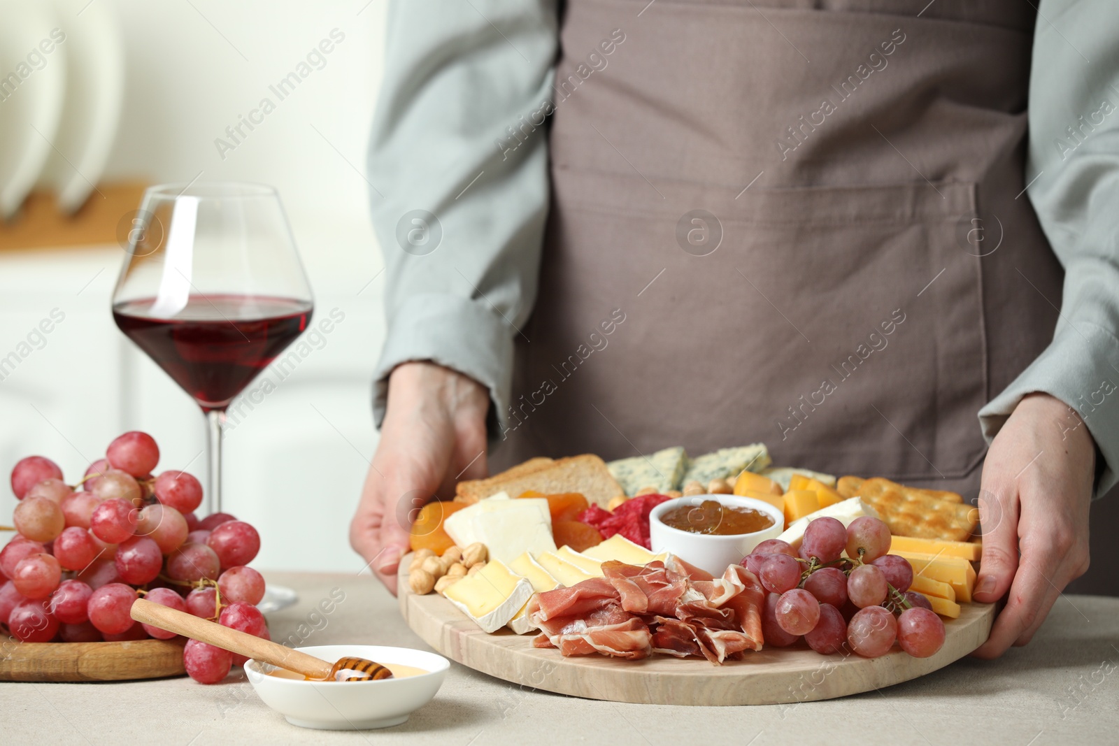 Photo of Woman holding board with different types of cut cheese and other snacks at light textured table, closeup