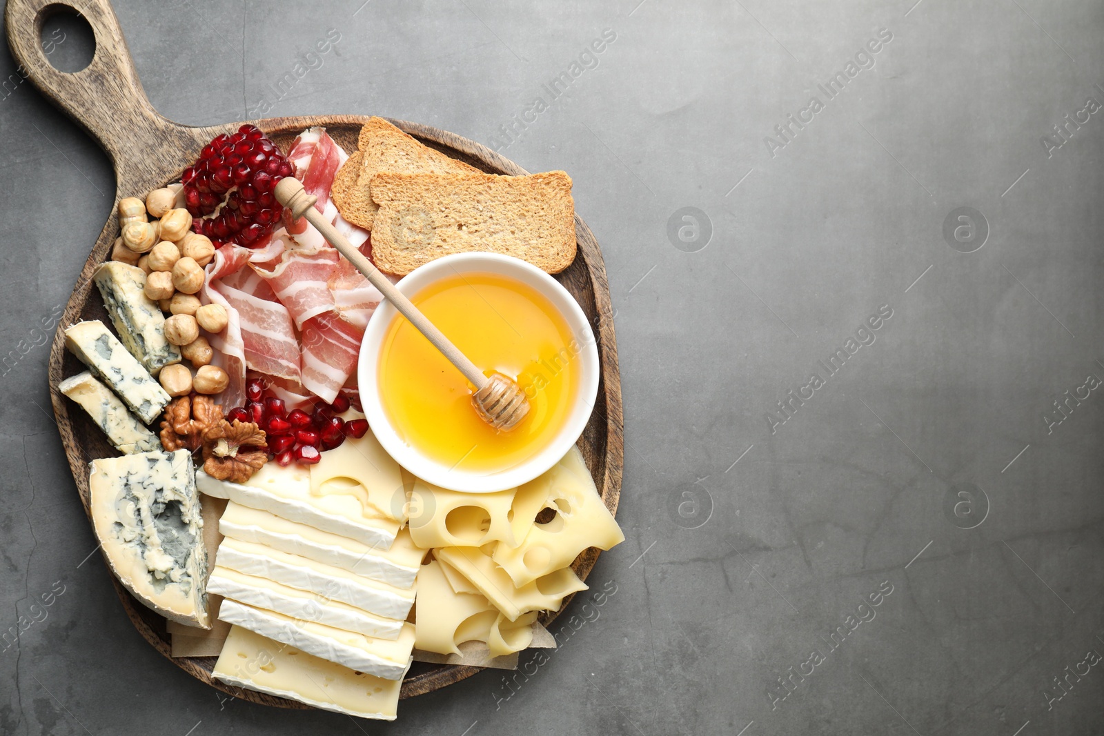 Photo of Different types of cut cheese and other snacks on gray textured table, top view. Space for text