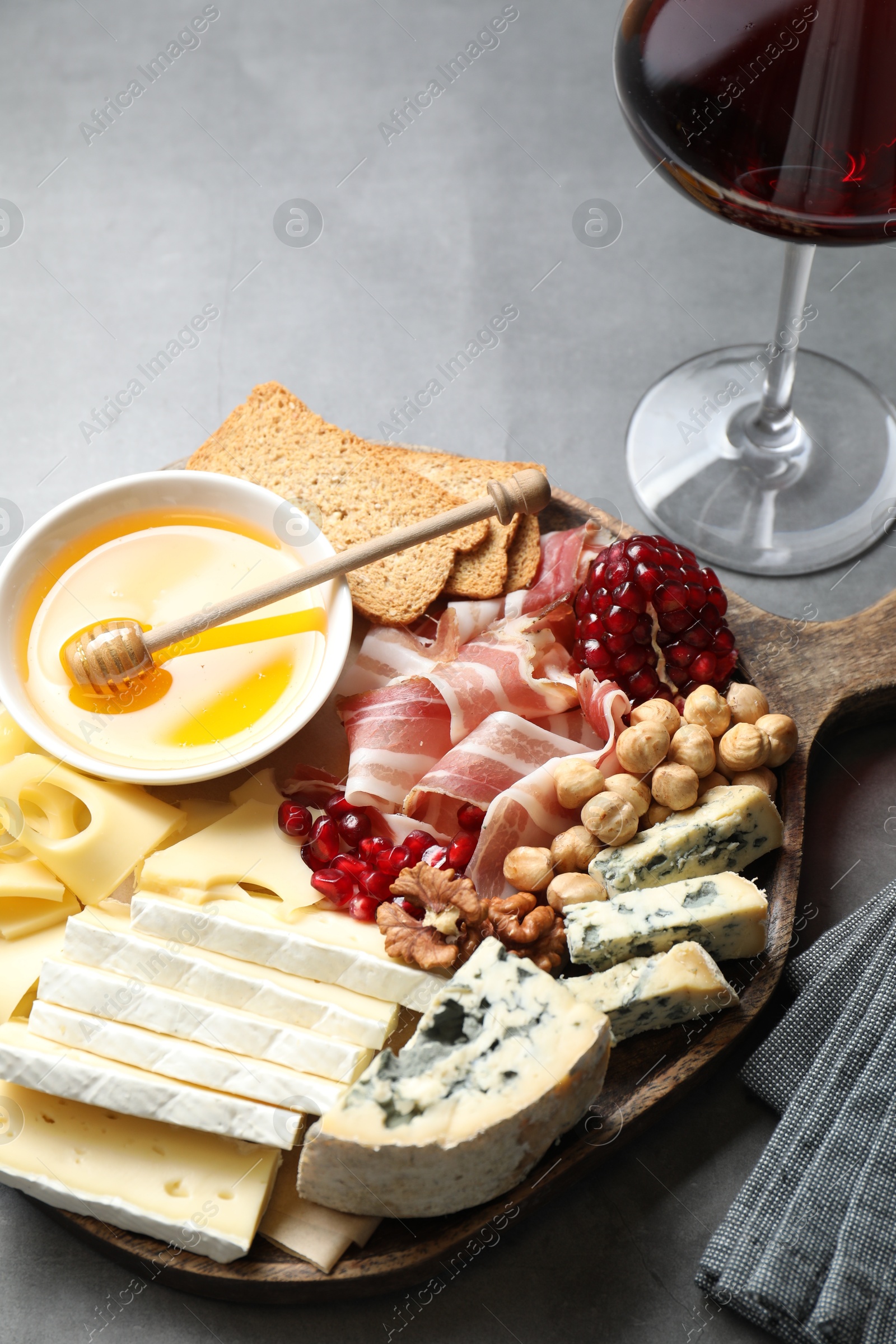 Photo of Different types of cut cheese and other snacks served with wine on gray table, closeup