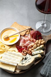 Photo of Different types of cut cheese and other snacks served with wine on gray table, closeup