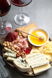 Photo of Different types of cut cheese and other snacks served with wine on gray table, closeup