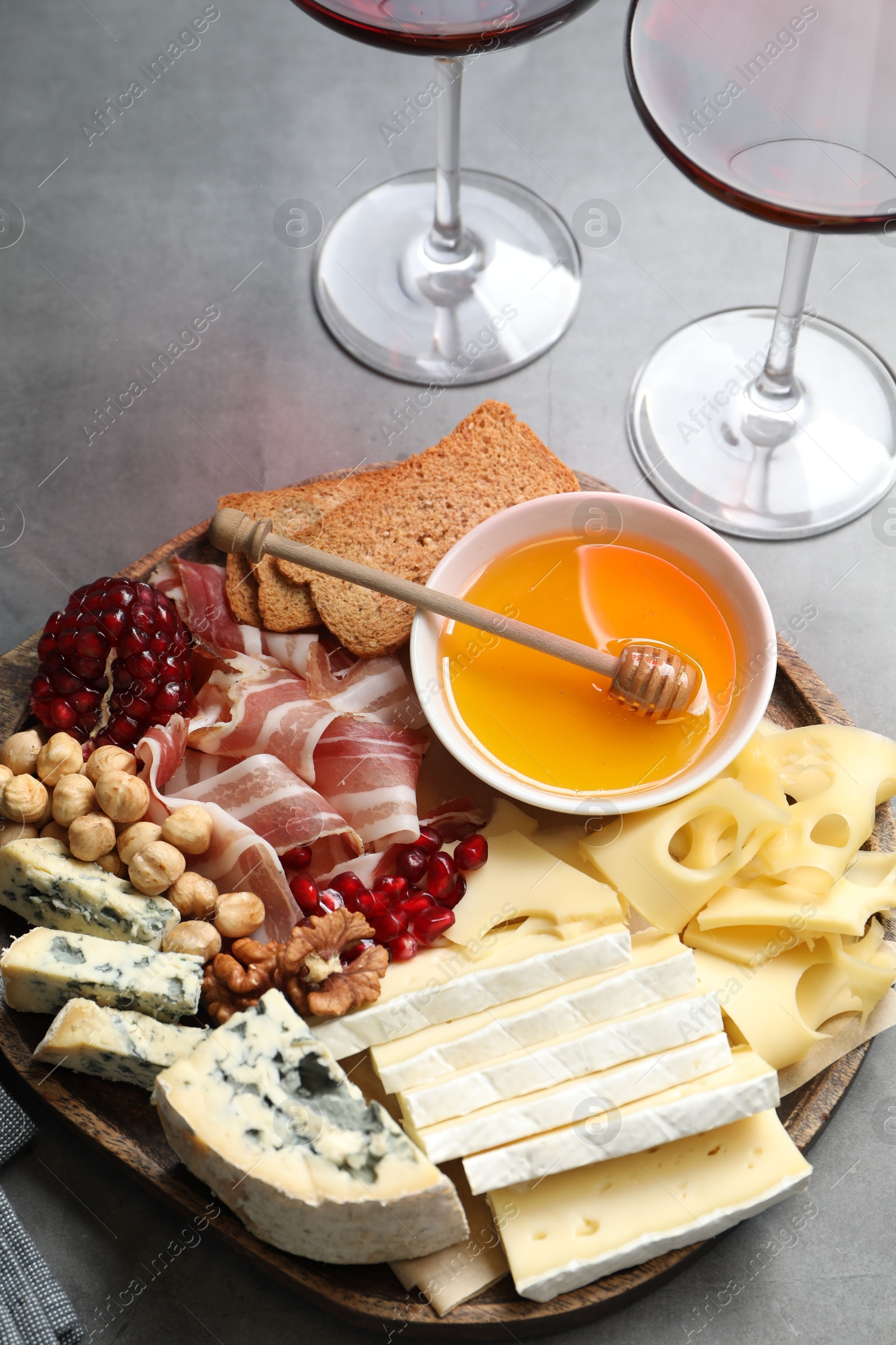 Photo of Different types of cut cheese and other snacks served with wine on gray table, closeup