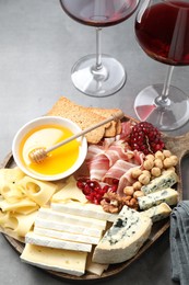 Photo of Different types of cut cheese and other snacks served with wine on gray table, closeup