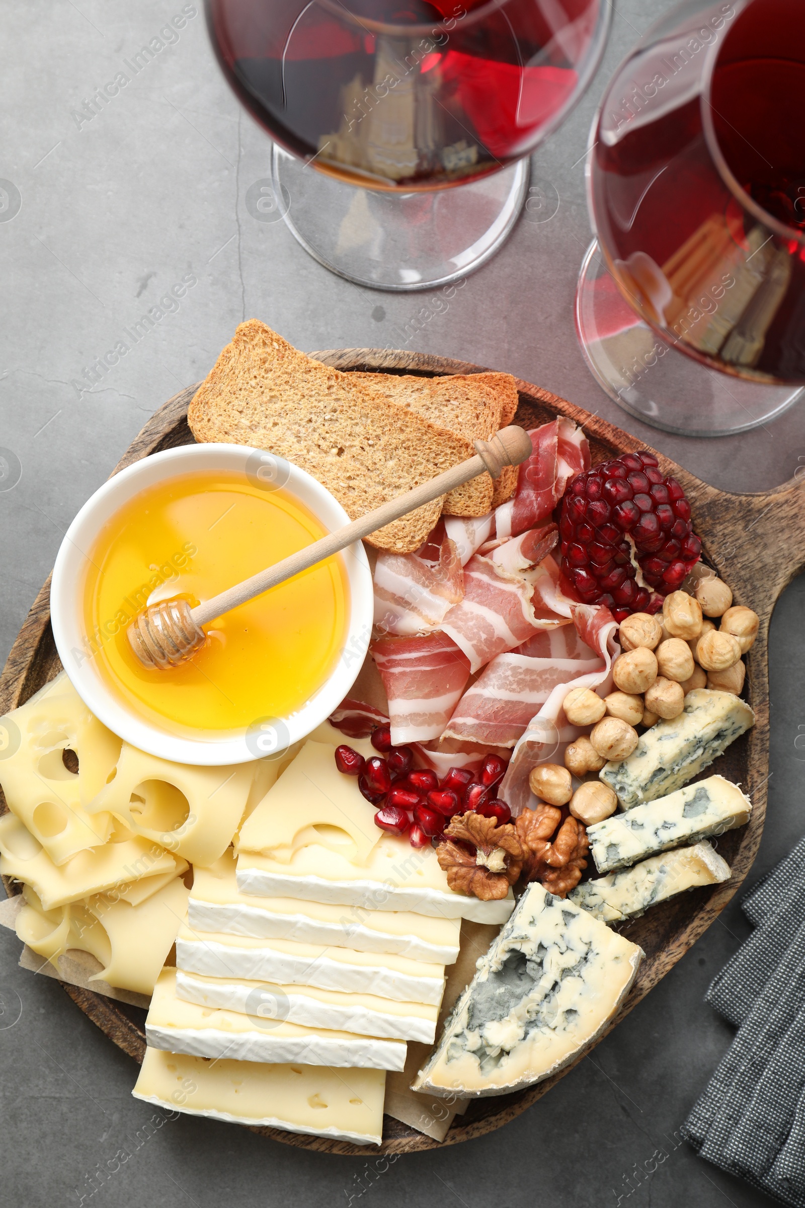 Photo of Different types of cut cheese and other snacks served with wine on gray textured table, flat lay