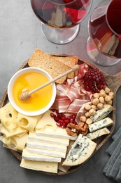 Photo of Different types of cut cheese and other snacks served with wine on gray textured table, flat lay