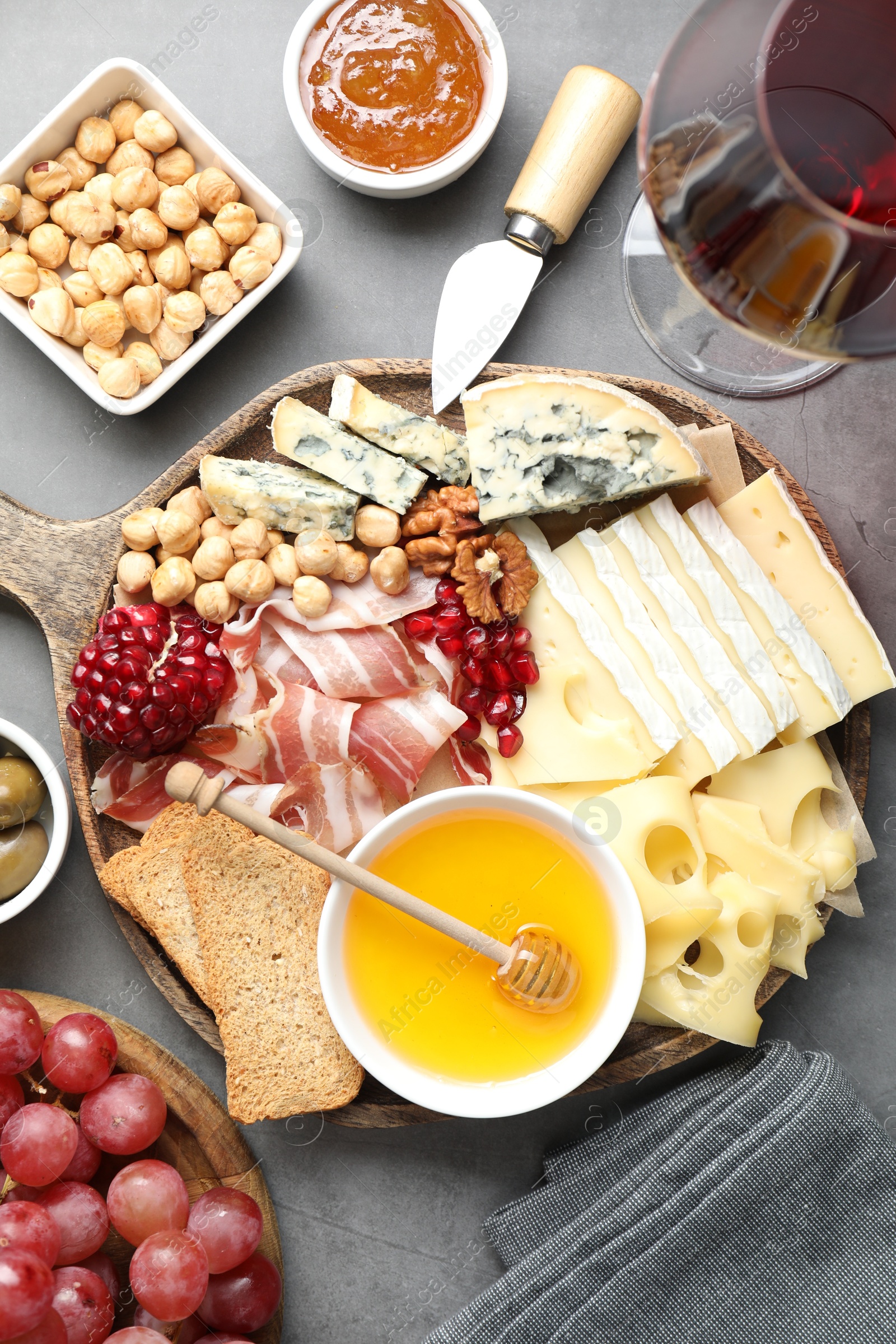 Photo of Different types of cut cheese and other snacks served with wine on gray textured table, flat lay