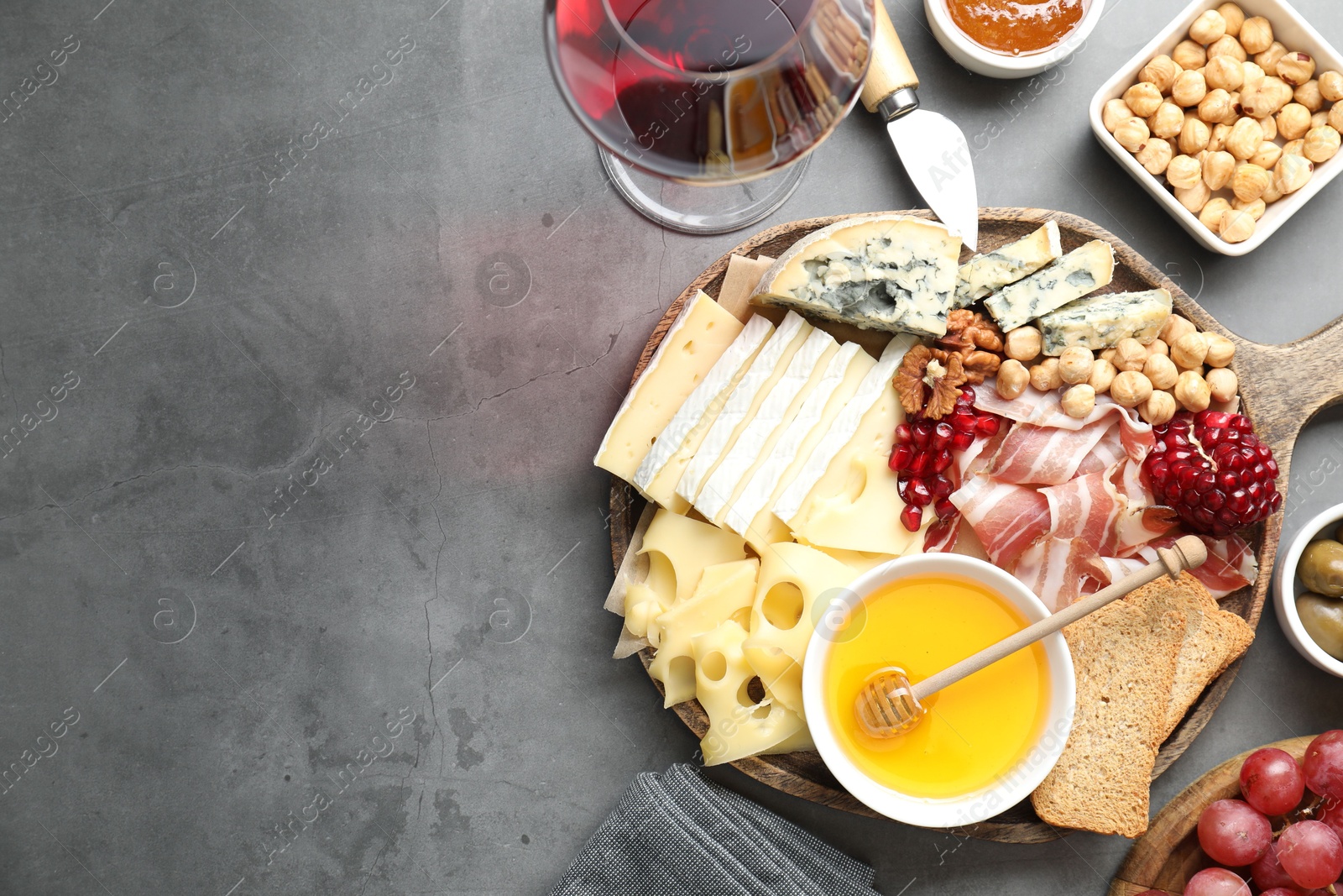 Photo of Different types of cut cheese and other snacks served with wine on gray textured table, flat lay. Space for text