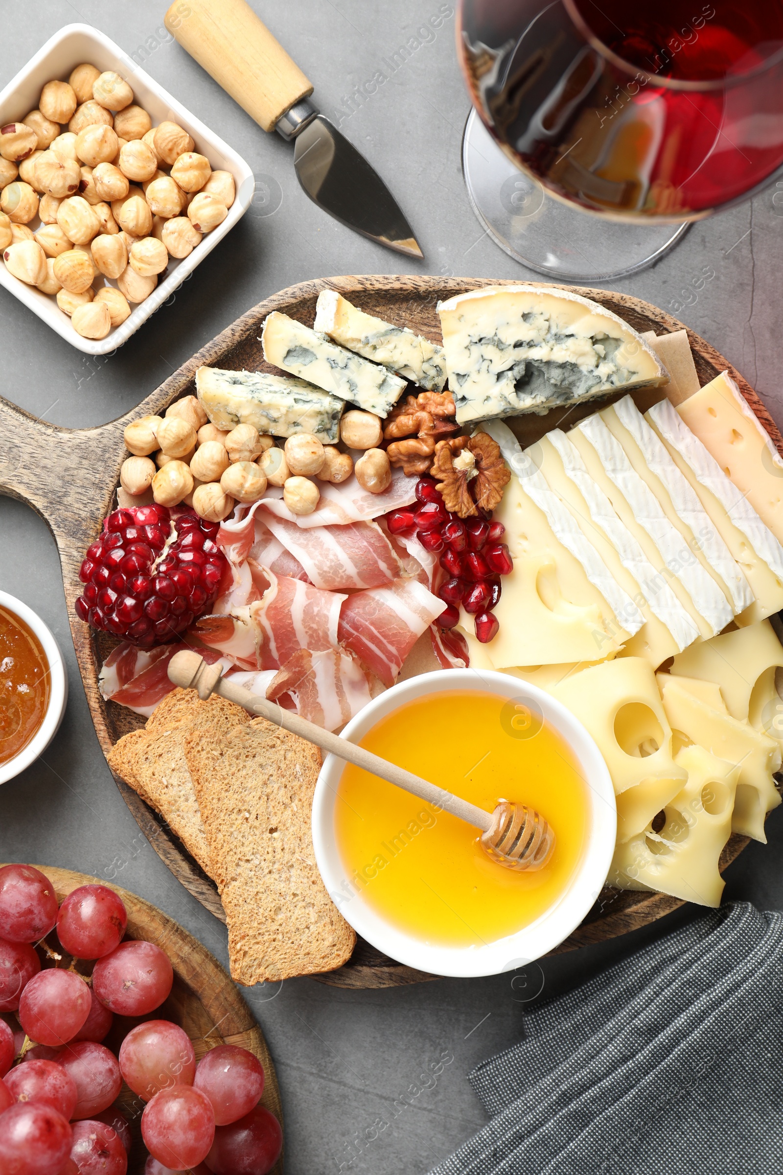 Photo of Different types of cut cheese and other snacks served with wine on gray textured table, flat lay