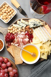 Photo of Different types of cut cheese and other snacks served with wine on gray textured table, flat lay