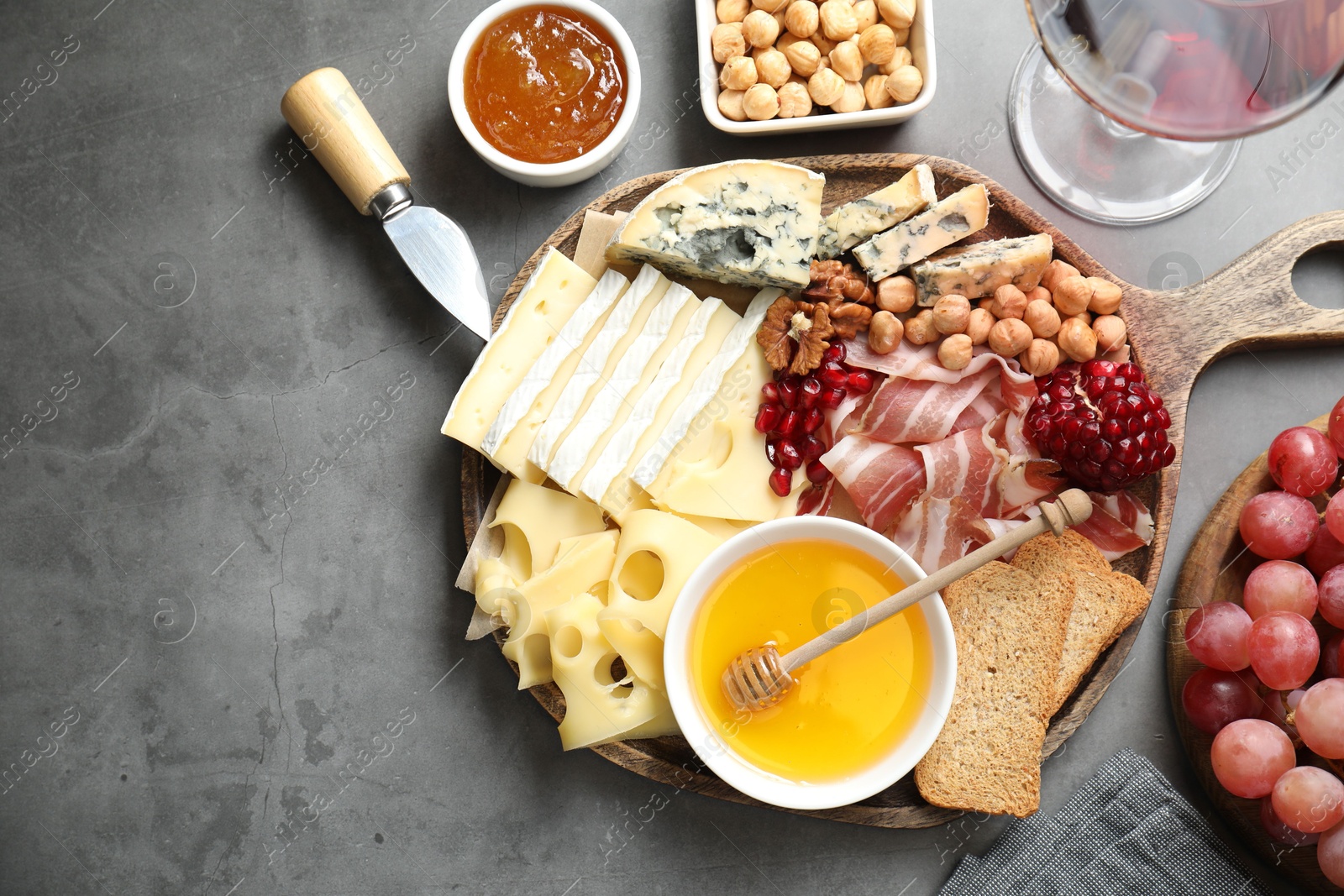 Photo of Different types of cut cheese and other snacks served with wine on gray textured table, flat lay. Space for text