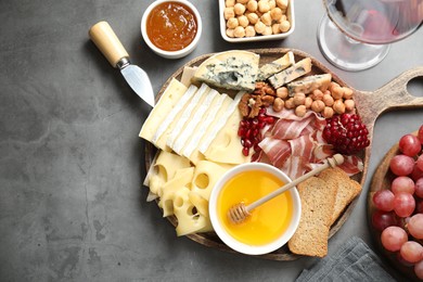 Photo of Different types of cut cheese and other snacks served with wine on gray textured table, flat lay. Space for text