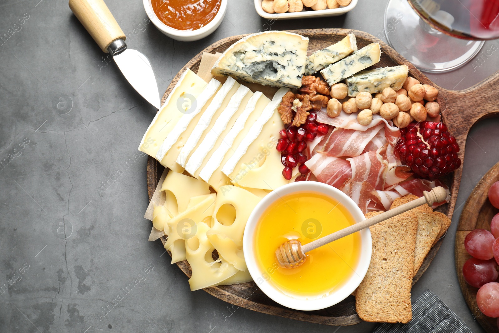 Photo of Different types of cut cheese and other snacks served with wine on gray textured table, flat lay. Space for text