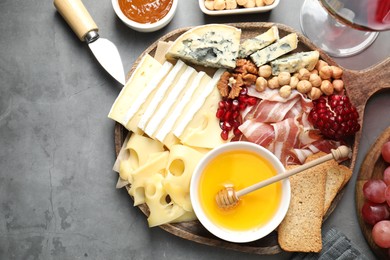 Photo of Different types of cut cheese and other snacks served with wine on gray textured table, flat lay. Space for text