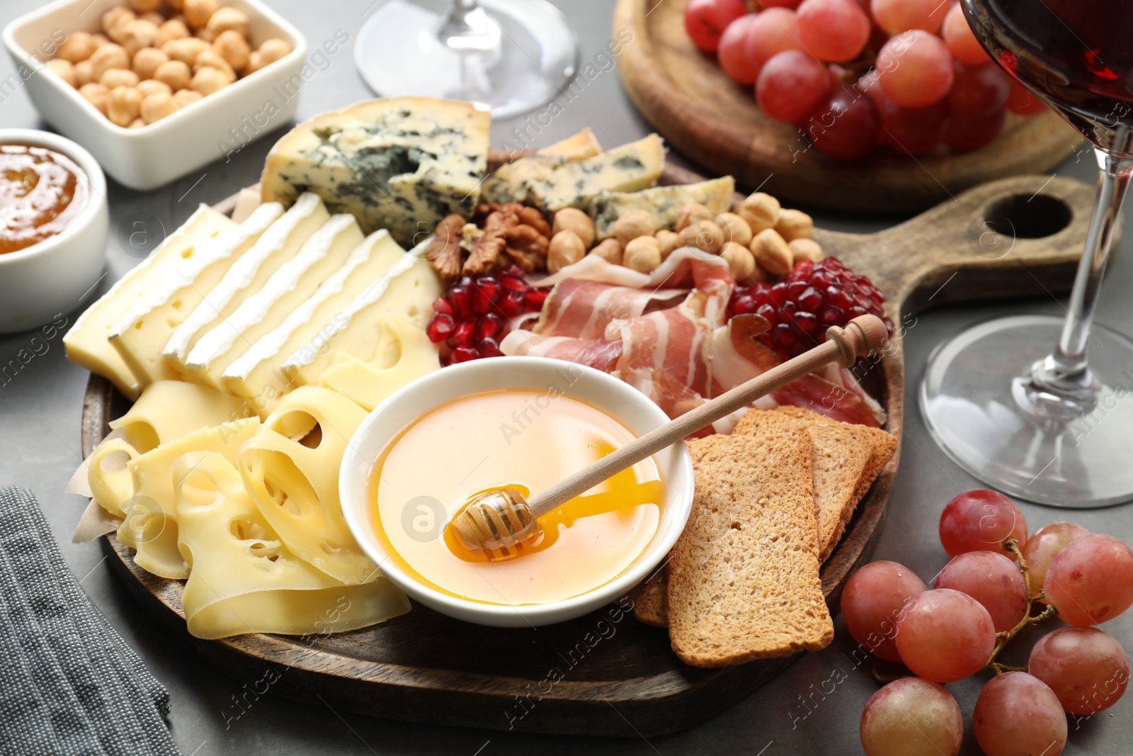 Photo of Different types of cut cheese and other snacks served with wine on gray table, closeup