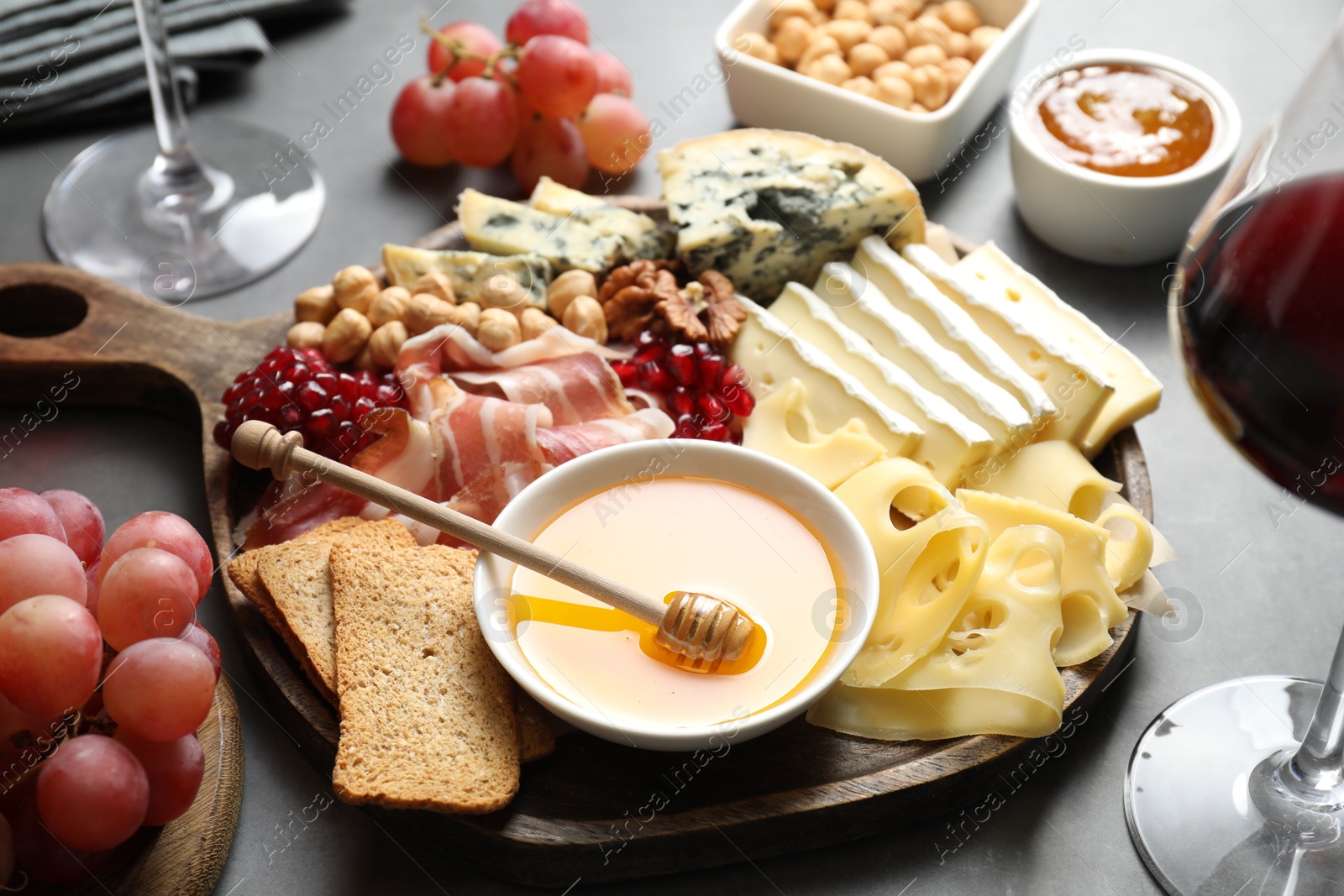 Photo of Different types of cut cheese and other snacks served with wine on gray table, closeup