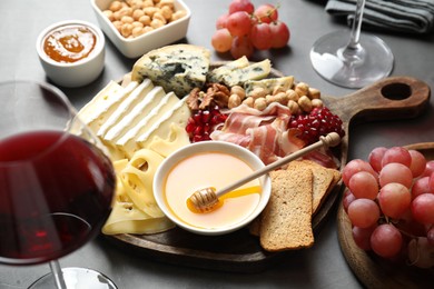 Photo of Different types of cut cheese and other snacks served with wine on gray table, closeup