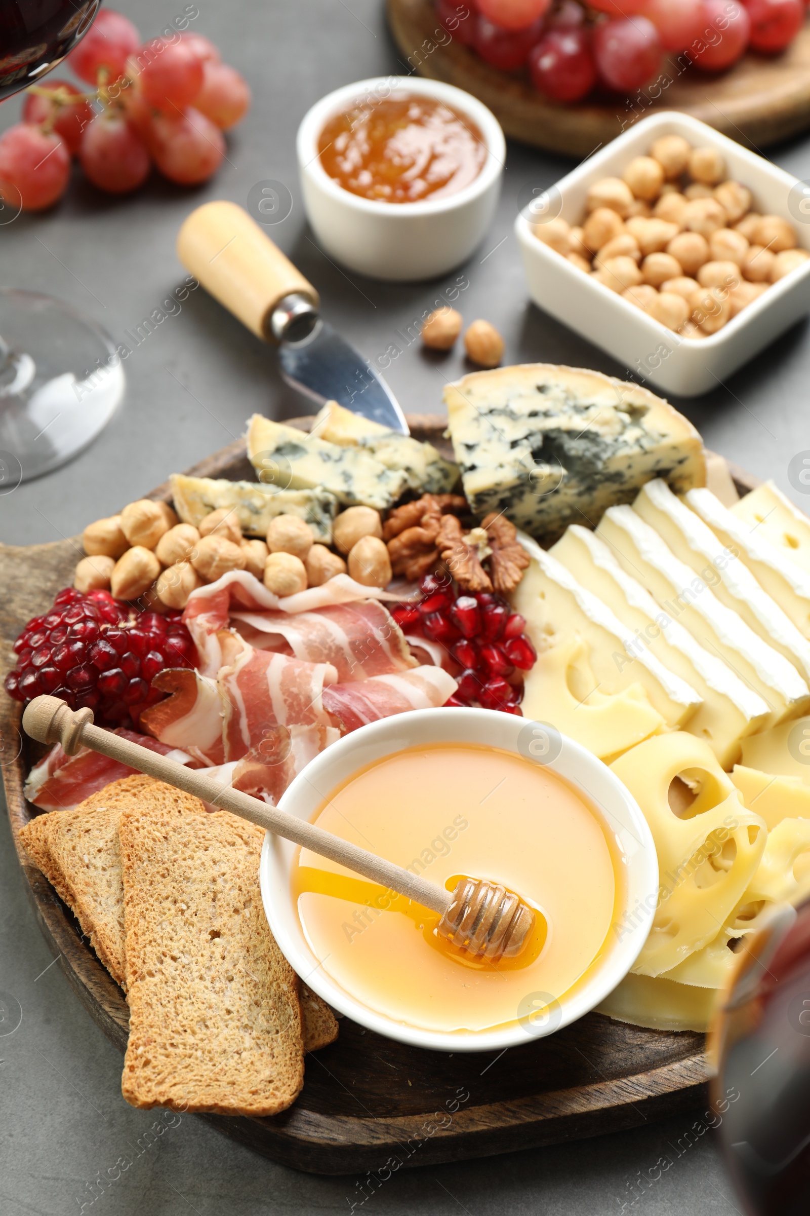 Photo of Different types of cut cheese and other snacks on gray table, closeup