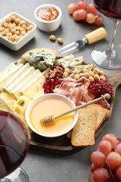 Photo of Different types of cut cheese and other snacks on gray textured table, closeup