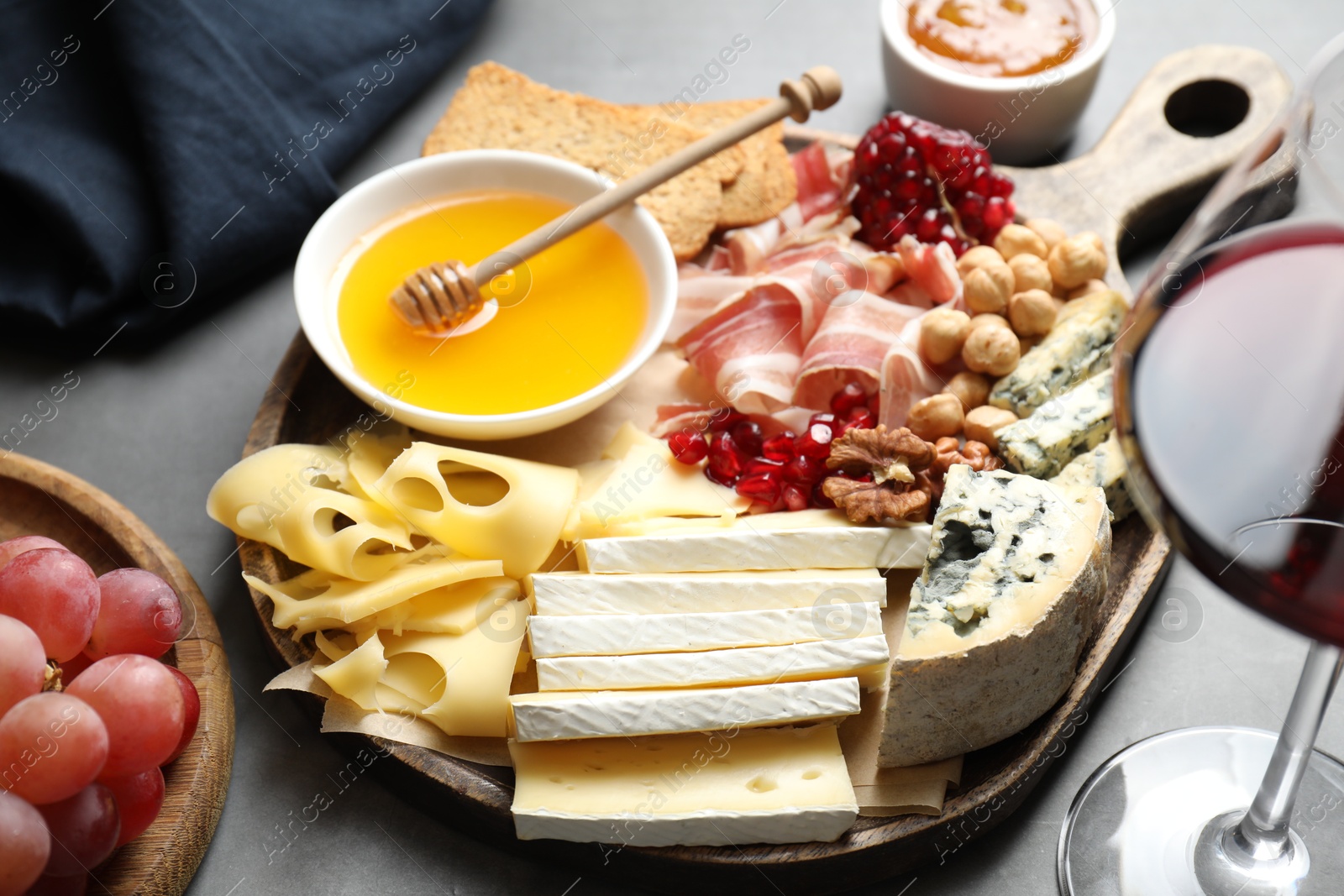 Photo of Different types of cut cheese and other snacks served with wine on gray table, closeup