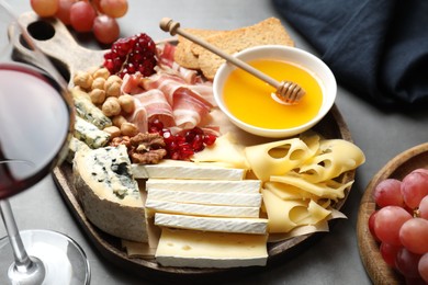 Photo of Different types of cut cheese and other snacks served with wine on gray table, closeup