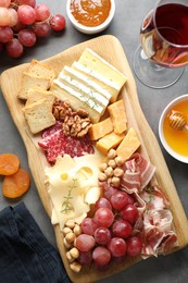 Photo of Different types of cut cheese and other snacks served with wine on gray textured table, flat lay