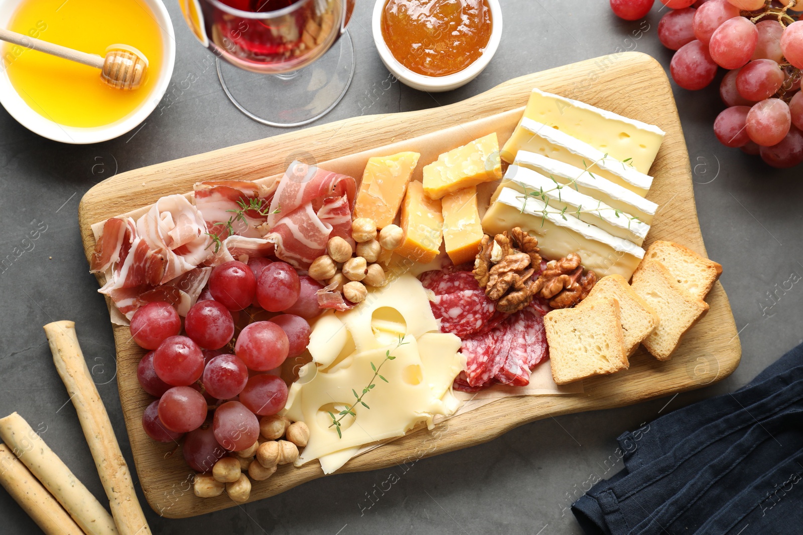 Photo of Different types of cut cheese and other snacks served with wine on gray textured table, flat lay