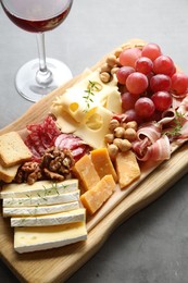 Photo of Different types of cut cheese and other snacks served with wine on gray textured table, closeup