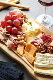 Photo of Different types of cut cheese and other snacks served with wine on gray table, closeup