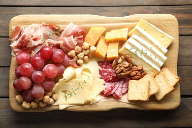 Photo of Different types of cut cheese and other snacks on wooden table, top view