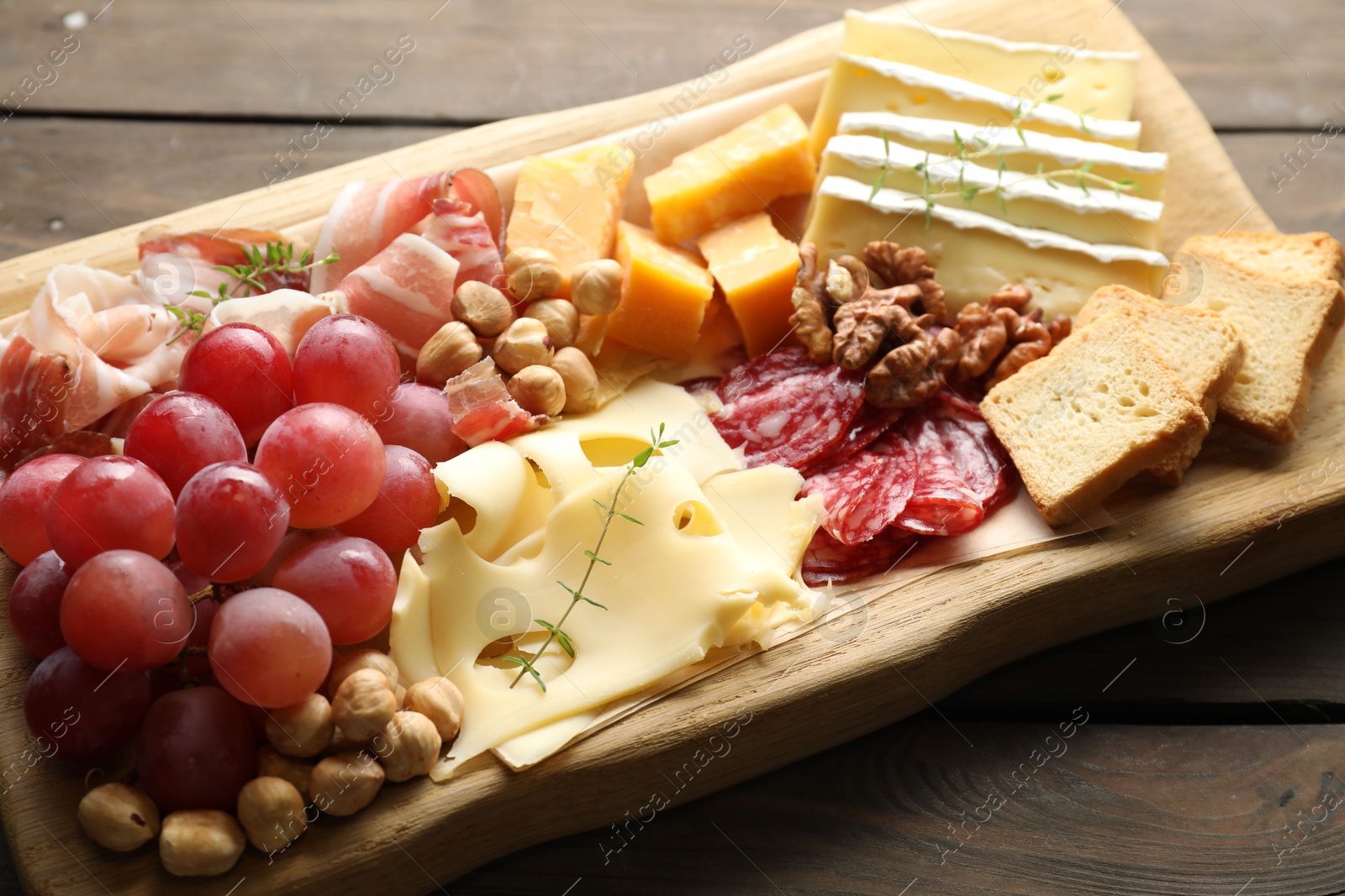 Photo of Different types of cut cheese and other snacks on wooden table, closeup