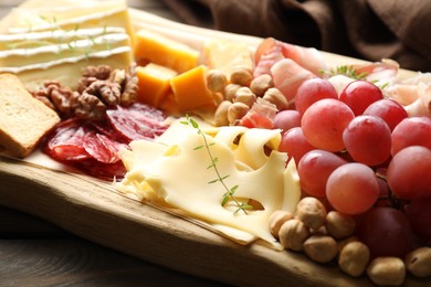 Photo of Different types of cut cheese and other snacks on wooden table, closeup