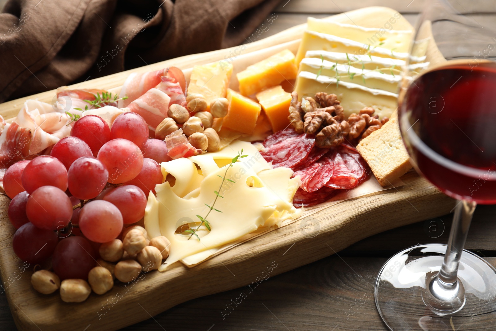 Photo of Different types of cut cheese and other snacks served with wine on wooden table, closeup