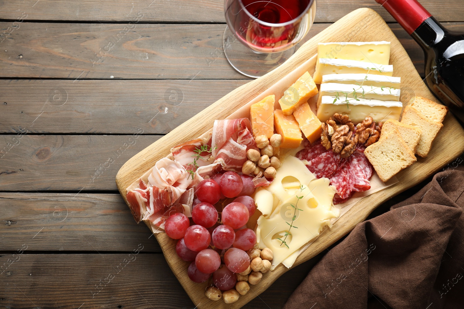 Photo of Different types of cut cheese and other snacks served with wine on wooden table, flat lay. Space for text