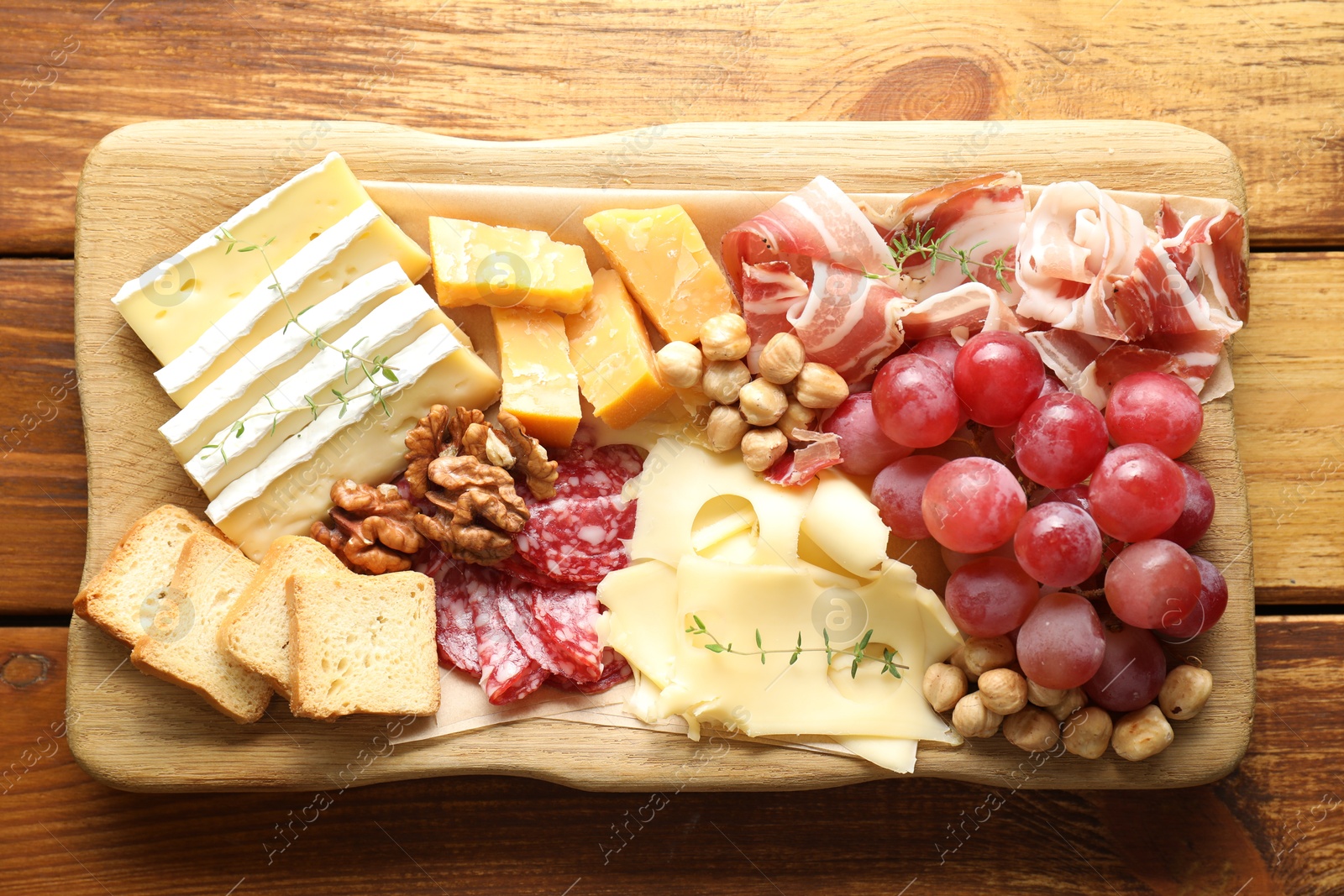 Photo of Different types of cut cheese and other snacks on wooden table, top view