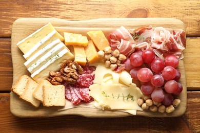 Photo of Different types of cut cheese and other snacks on wooden table, top view