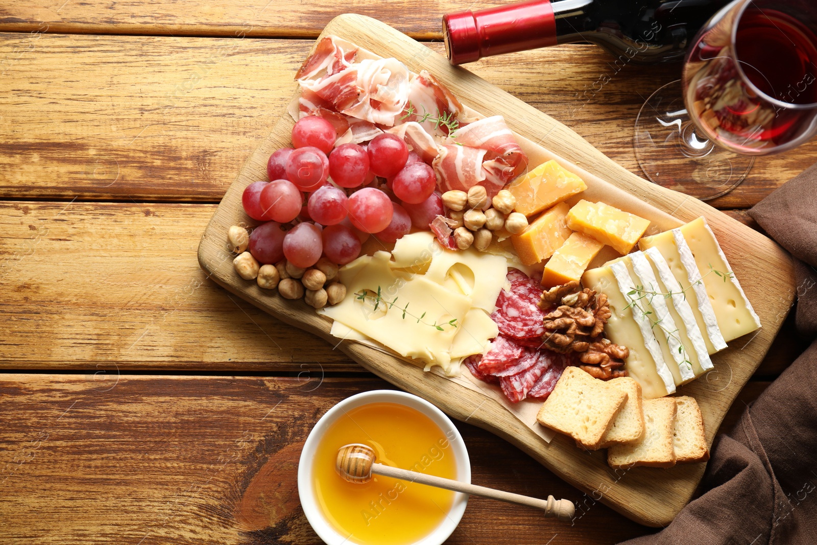 Photo of Different types of cut cheese and other snacks served with wine on wooden table, flat lay. Space for text