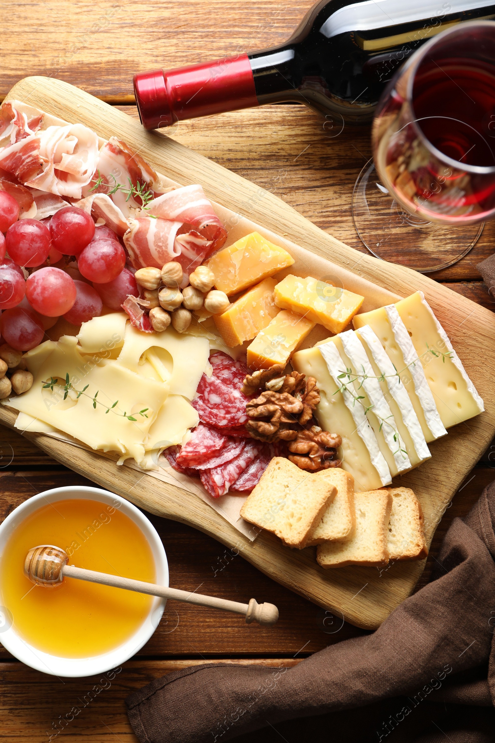 Photo of Different types of cut cheese and other snacks served with wine on wooden table, flat lay