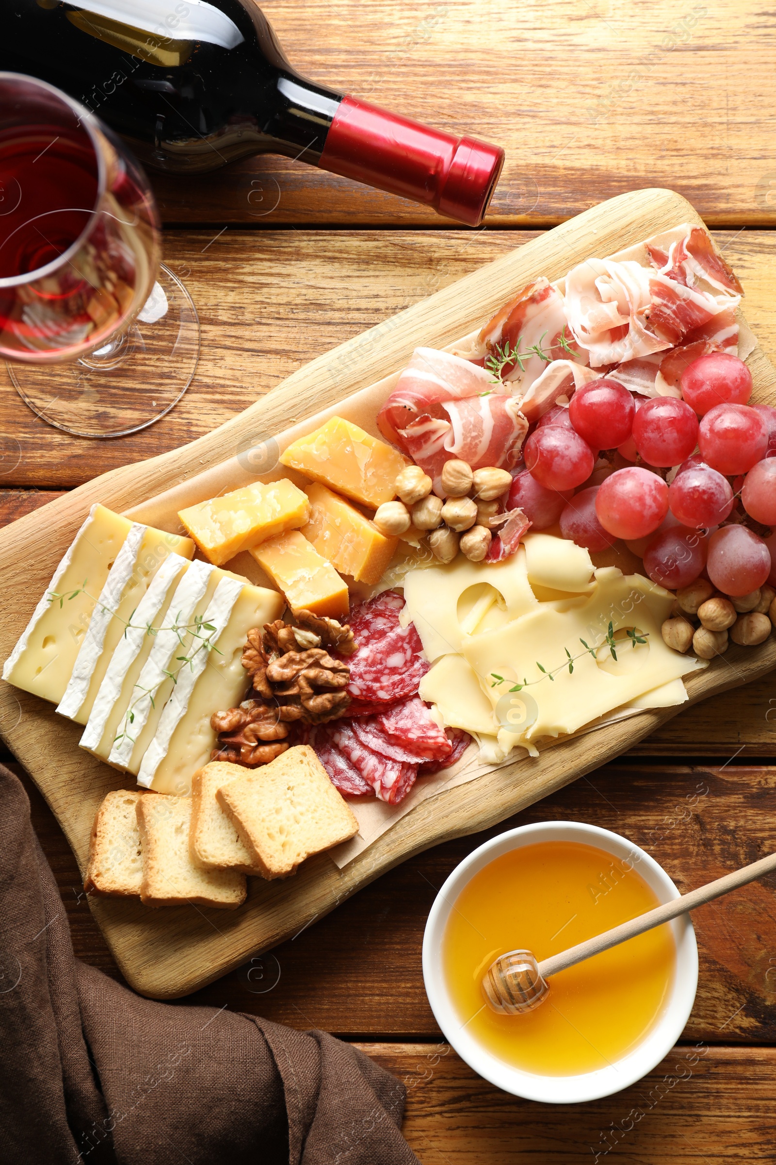 Photo of Different types of cut cheese and other snacks served with wine on wooden table, flat lay