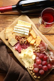 Photo of Different types of cut cheese and other snacks served with wine on wooden table, flat lay