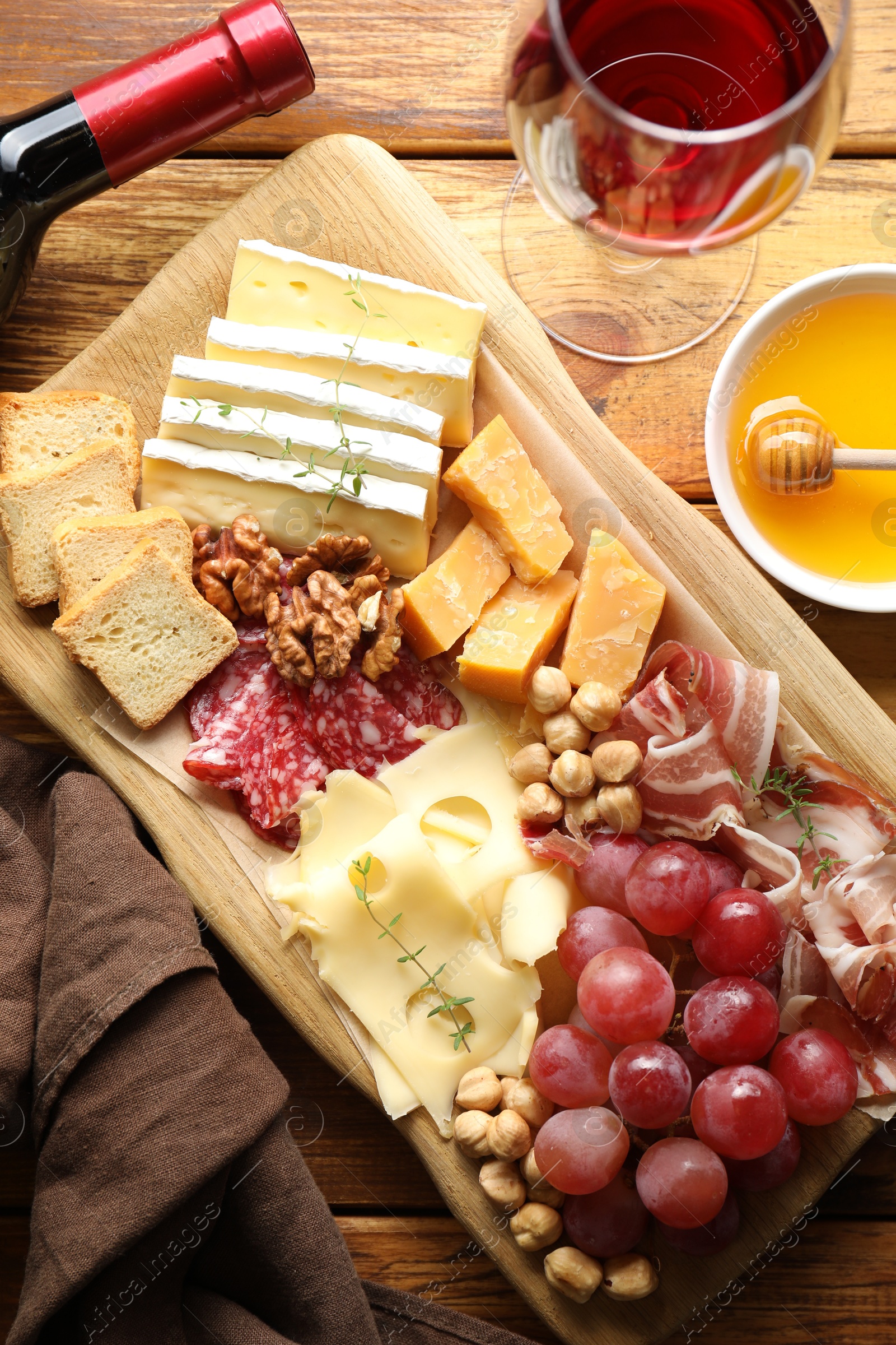 Photo of Different types of cut cheese and other snacks served with wine on wooden table, flat lay