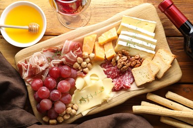 Photo of Different types of cut cheese and other snacks served with wine on wooden table, flat lay