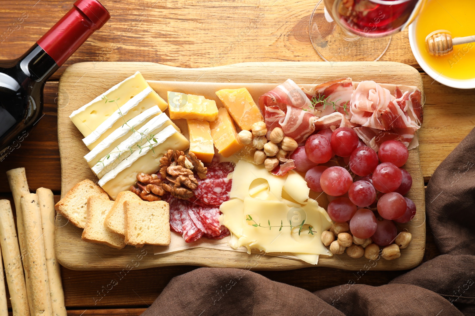 Photo of Different types of cut cheese and other snacks served with wine on wooden table, flat lay