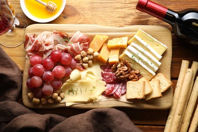 Photo of Different types of cut cheese and other snacks served with wine on wooden table, flat lay