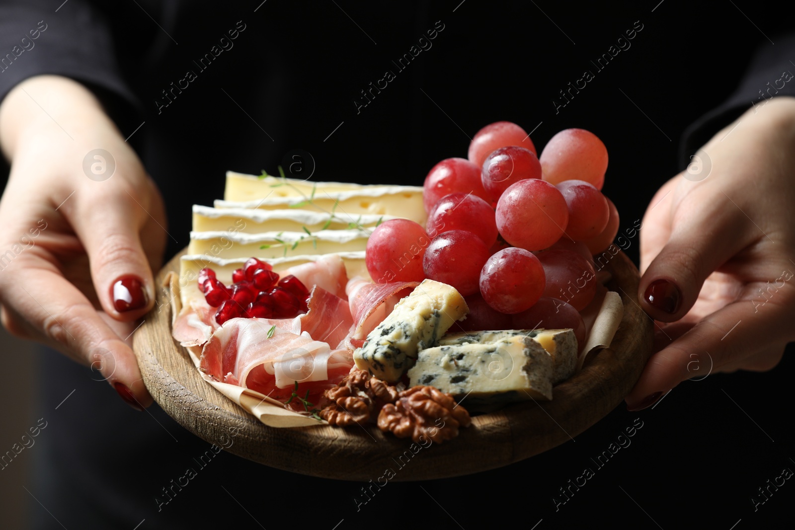 Photo of Woman holding board with different types of delicious cheese and other snacks, closeup