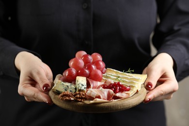 Photo of Woman holding board with different types of delicious cheese and other snacks, closeup