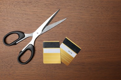 Photo of Pieces of cut credit card and scissors on wooden table, top view